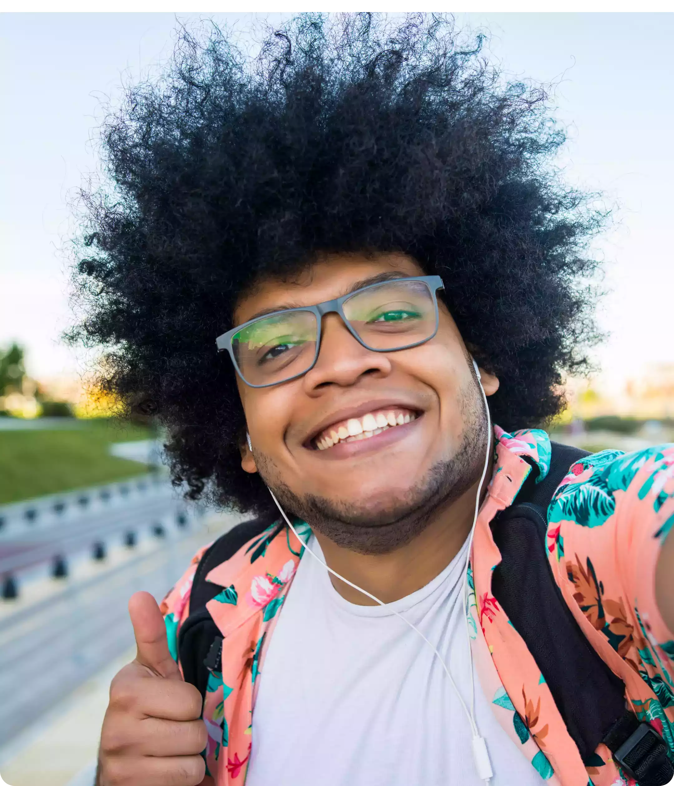 Jeune homme souriant avec des lunettes, levant le pouce en l'air après avoir réussi son permis de conduire, en extérieur.
