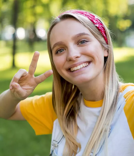 Jeune femme souriante faisant un signe de paix après avoir réussi son permis de conduire, en extérieur